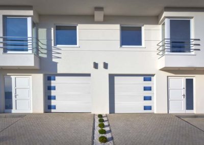 Two sleek white modern residential garage doors with striking blue-tinted horizontal windows, enhancing a contemporary multi-unit dwelling