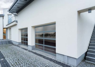 Contemporary white building featuring two glass garage doors, reflecting scenery with a clean, sleek design